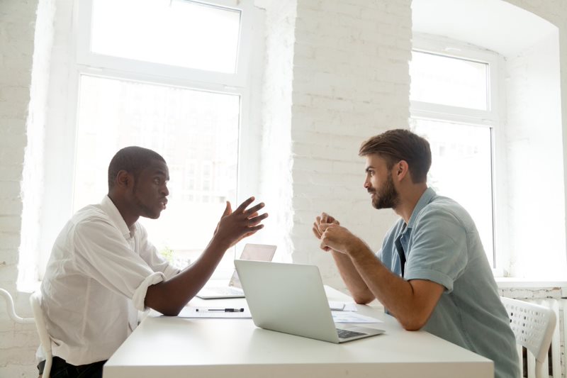 two people talking with a laptop on the desk