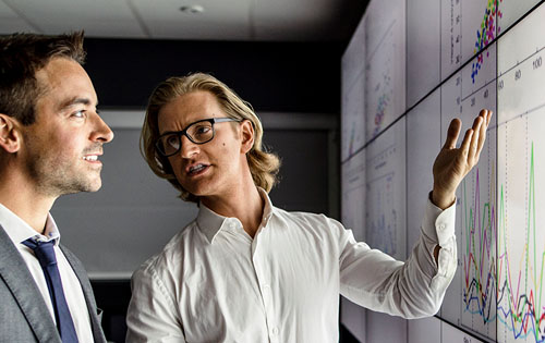 two people discussing and looking at the screen with graphs on it