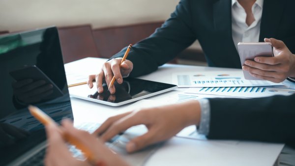 two people working with laptops, tablet and papers on the table