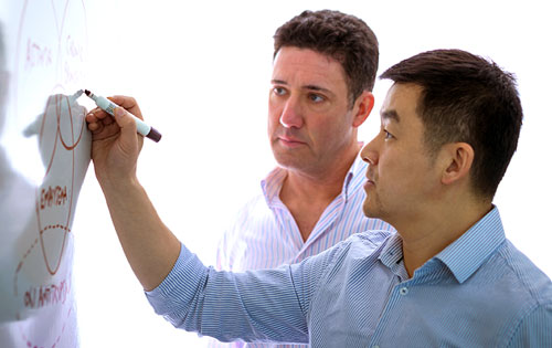 two people working and drawing on the white board